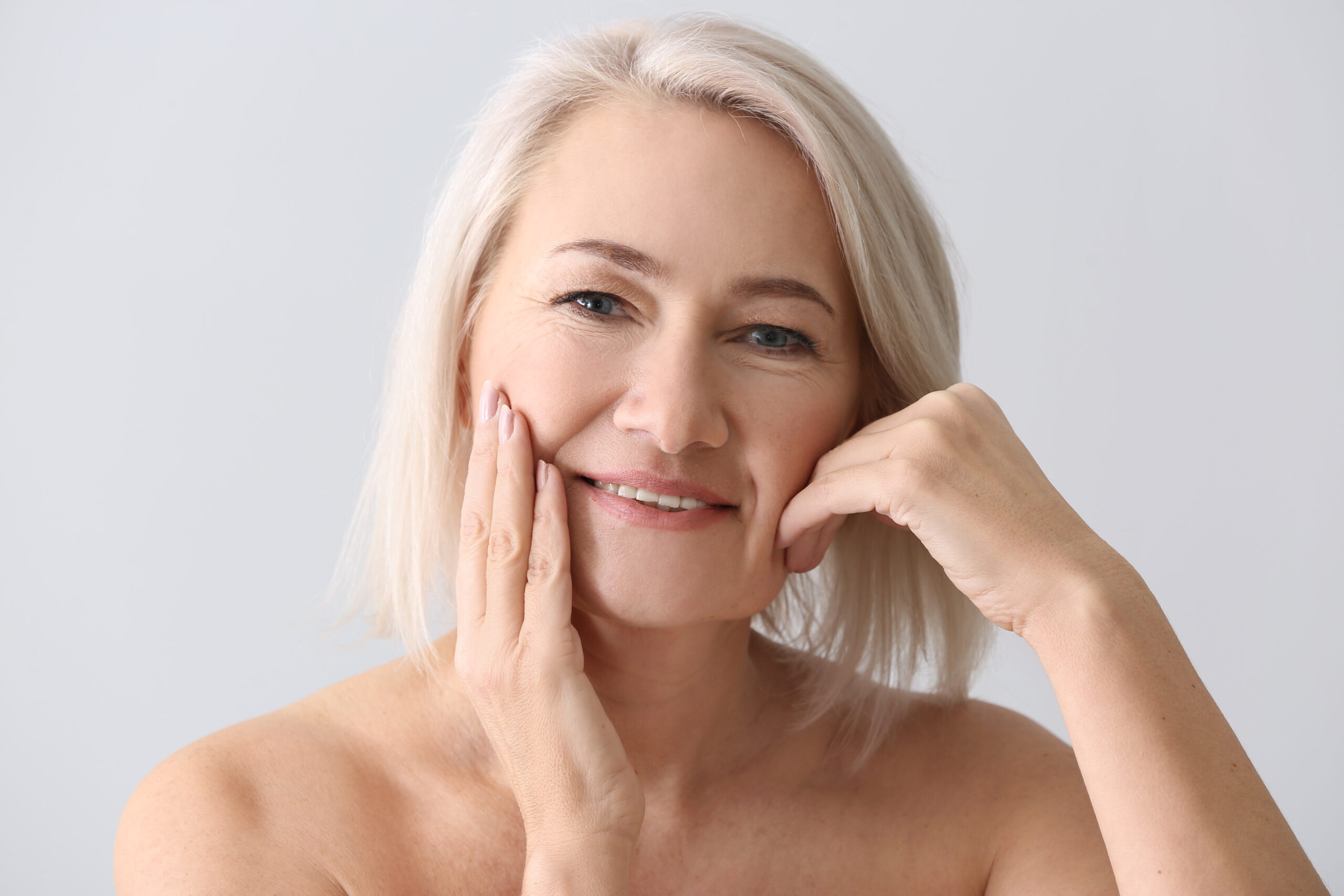 Mature woman giving herself face massage on light background