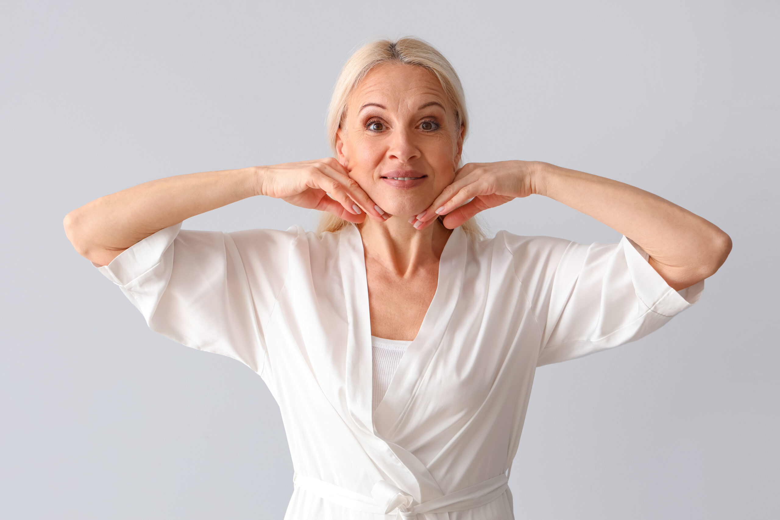 Mature woman doing face building exercise on light background